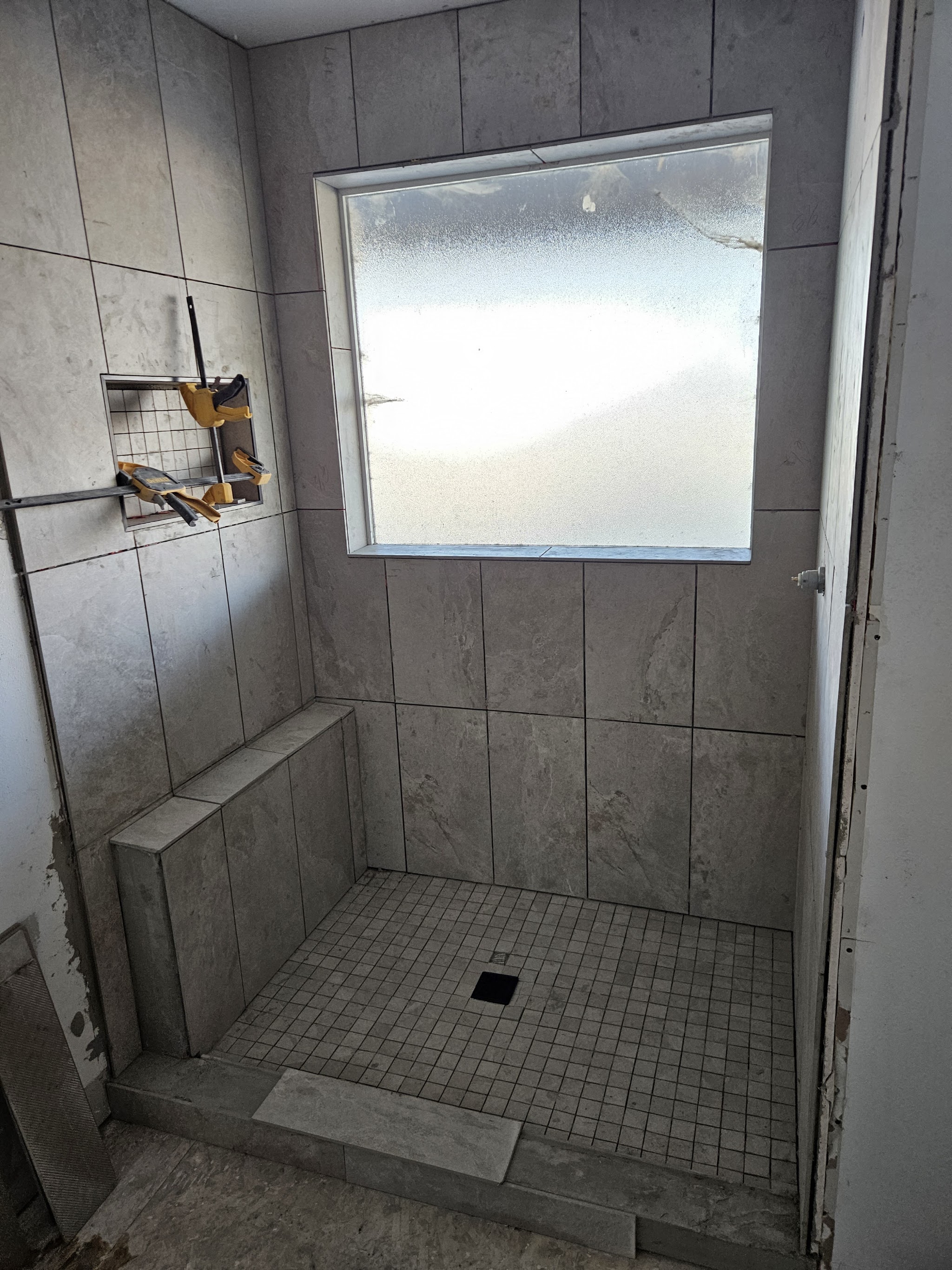 Tiled walk in shower with a built in bench and recessed niche in gray stone look tile