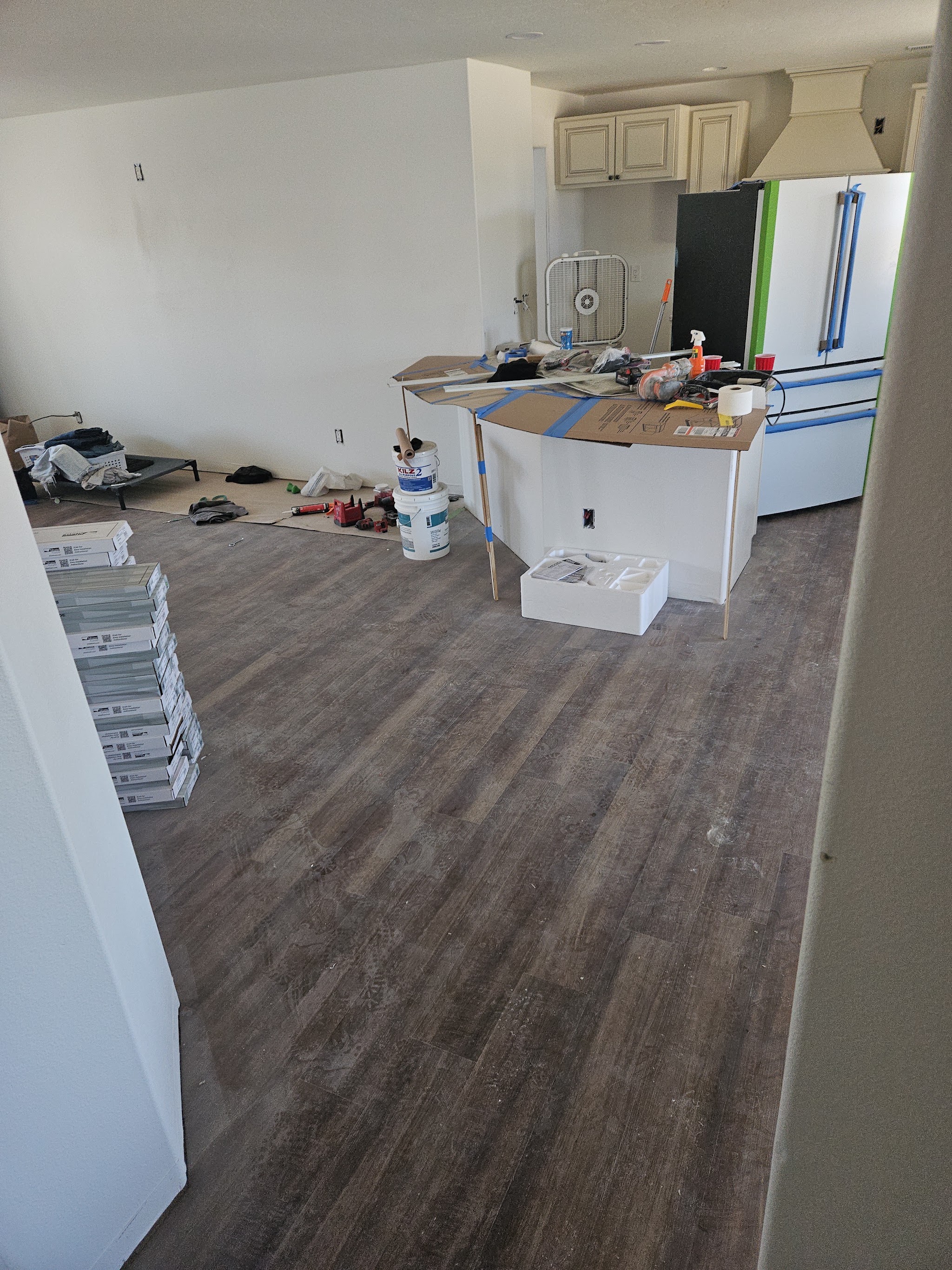 Kitchen and living room remodel underway with new plank flooring laid and cabinets masked off